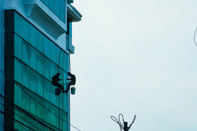 Two window cleaners work on a tall building.